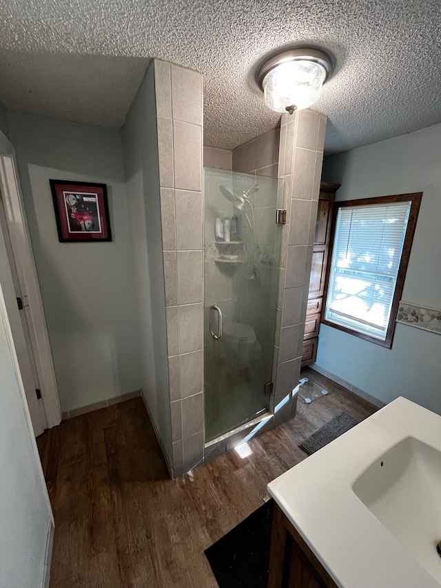 bathroom featuring wood finished floors, a textured ceiling, a stall shower, and vanity