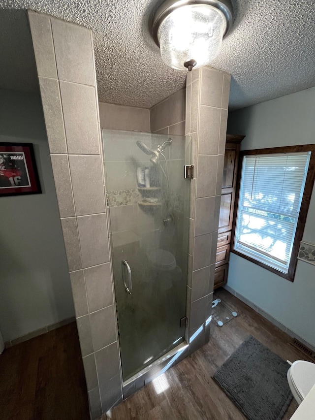 full bathroom with wood finished floors, a stall shower, toilet, and a textured ceiling