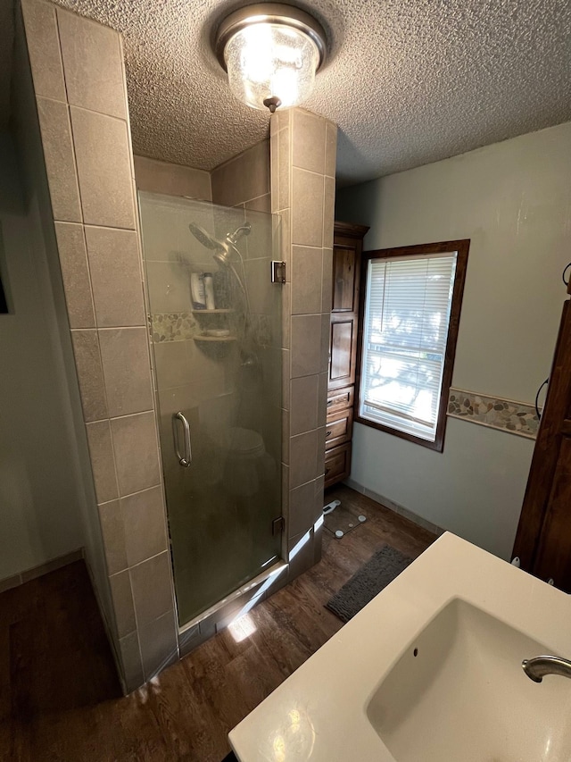 bathroom featuring a sink, wood finished floors, a stall shower, and a textured ceiling