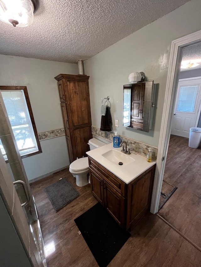 bathroom with wood finished floors, a textured ceiling, vanity, healthy amount of natural light, and toilet