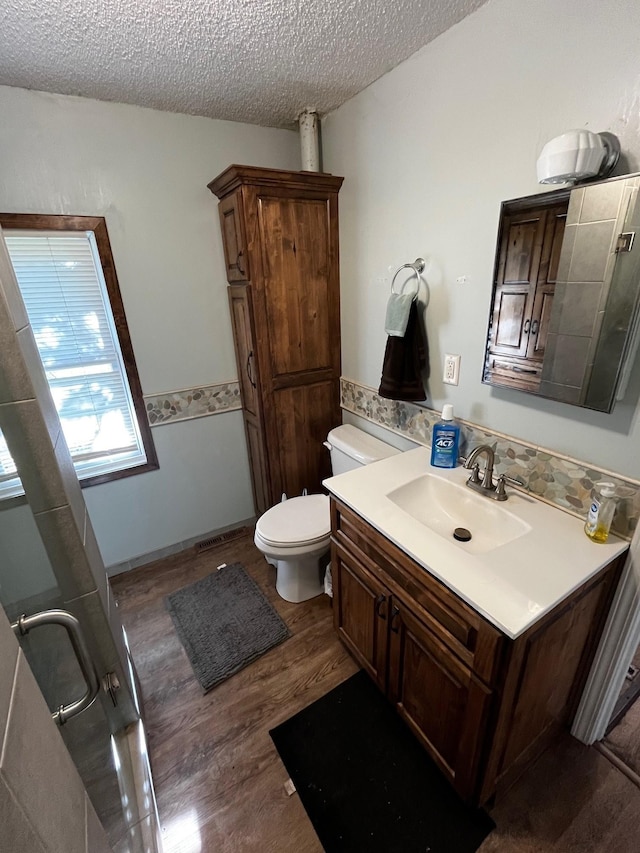 bathroom with wood finished floors, a textured ceiling, toilet, vanity, and a shower with shower door
