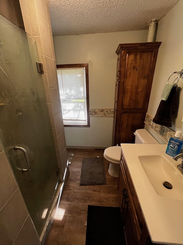 bathroom featuring wood finished floors, toilet, a textured ceiling, a shower stall, and vanity
