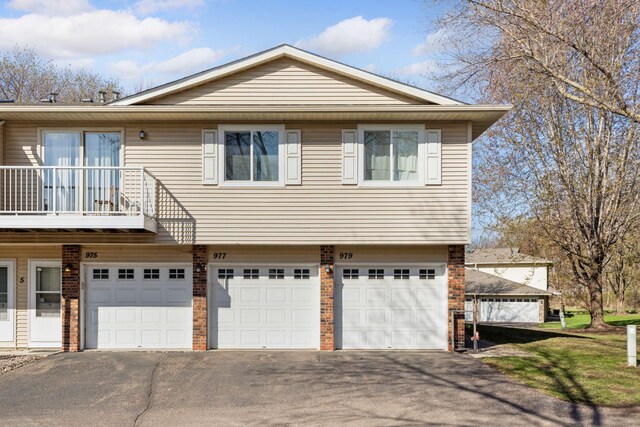 view of front facade featuring an attached garage, aphalt driveway, a balcony, and brick siding