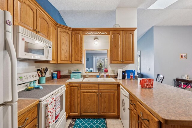 kitchen featuring a sink, white appliances, brown cabinetry, a peninsula, and a skylight