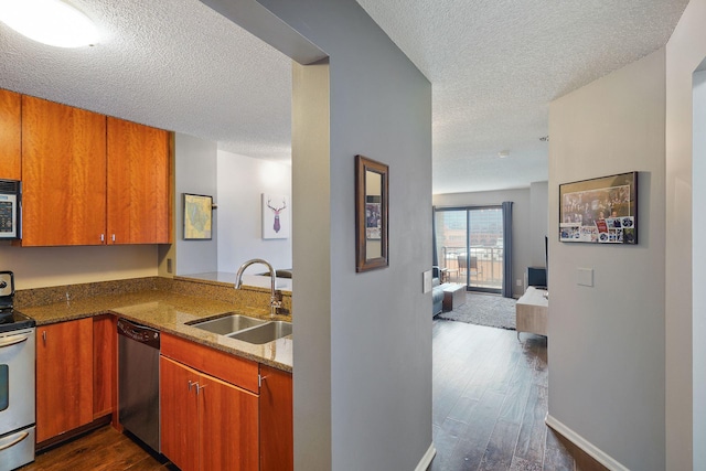 kitchen featuring stone countertops, dark wood-style floors, a textured ceiling, a sink, and appliances with stainless steel finishes