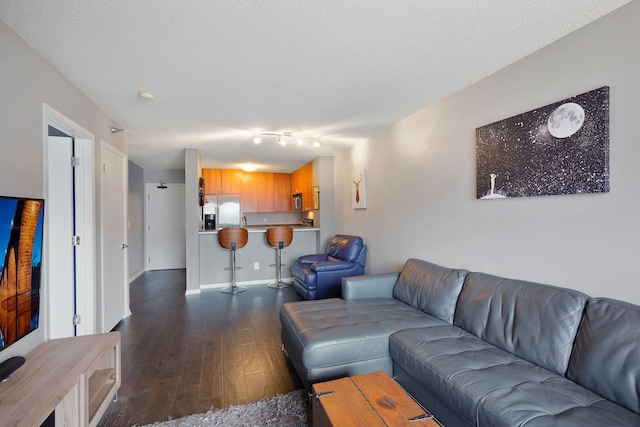 living area with track lighting, a textured ceiling, dark wood-style floors, and baseboards