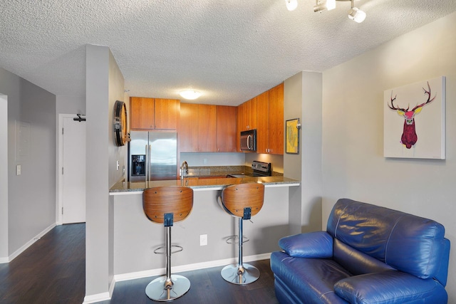 kitchen with dark wood-style flooring, a peninsula, brown cabinets, and stainless steel appliances
