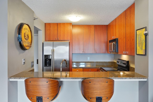 kitchen featuring brown cabinetry, a peninsula, a textured ceiling, and appliances with stainless steel finishes