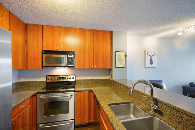 kitchen featuring a sink, a textured ceiling, brown cabinets, and stainless steel appliances