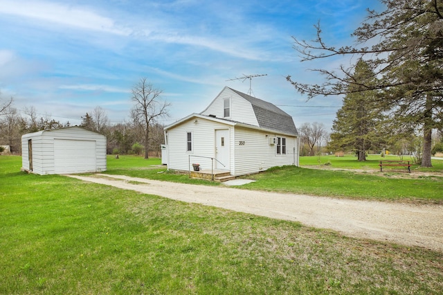 view of side of property featuring dirt driveway, a lawn, a detached garage, an outdoor structure, and a gambrel roof