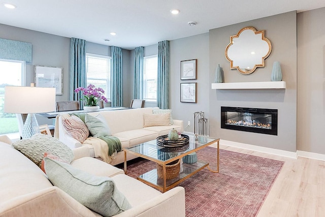 living room with a glass covered fireplace, baseboards, recessed lighting, and wood finished floors