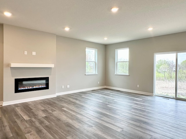 unfurnished living room with a textured ceiling, wood finished floors, baseboards, a glass covered fireplace, and recessed lighting