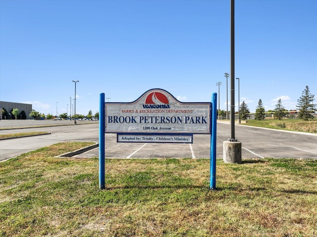 community sign featuring a lawn and uncovered parking