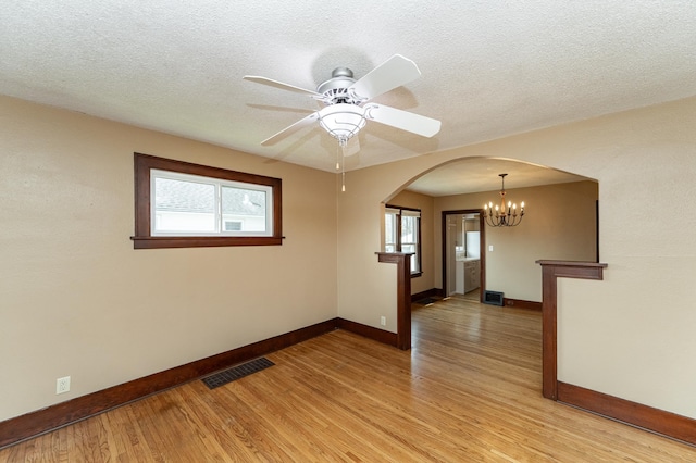 spare room featuring baseboards, arched walkways, light wood-style flooring, and visible vents