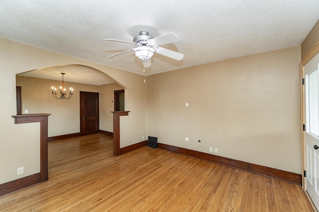 empty room with light wood finished floors, arched walkways, a textured ceiling, ceiling fan with notable chandelier, and baseboards
