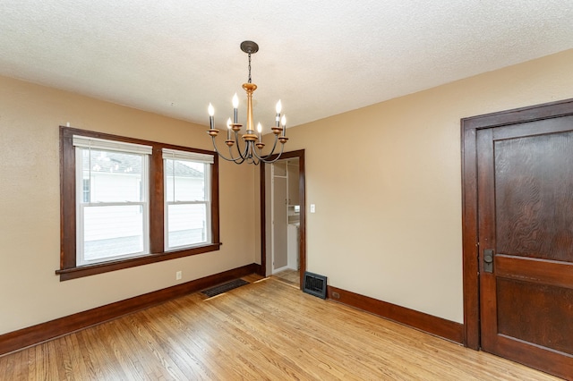 empty room with baseboards, an inviting chandelier, visible vents, and light wood-style floors