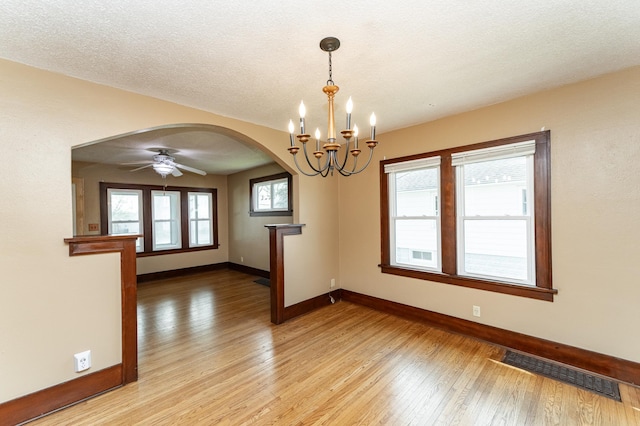 unfurnished room featuring visible vents, baseboards, arched walkways, light wood-style flooring, and ceiling fan with notable chandelier