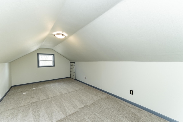 additional living space featuring baseboards, vaulted ceiling, and light carpet
