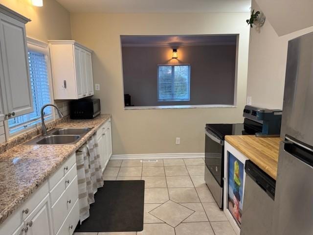 kitchen with a sink, light tile patterned floors, baseboards, white cabinets, and stainless steel appliances