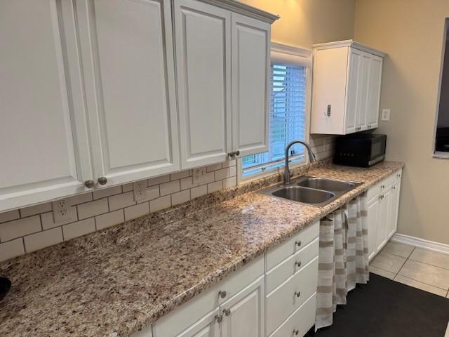 kitchen with decorative backsplash, black microwave, a sink, baseboards, and white cabinetry
