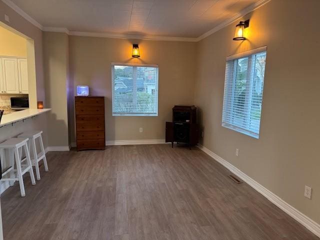 unfurnished dining area featuring baseboards, ornamental molding, a wood stove, and dark wood finished floors