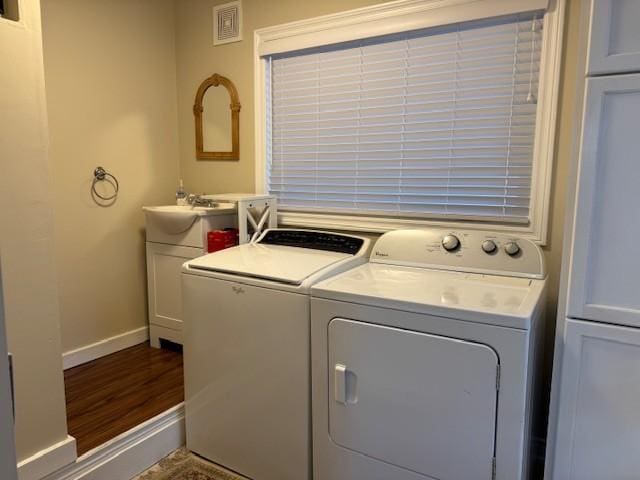 clothes washing area featuring cabinet space, wood finished floors, a sink, baseboards, and separate washer and dryer