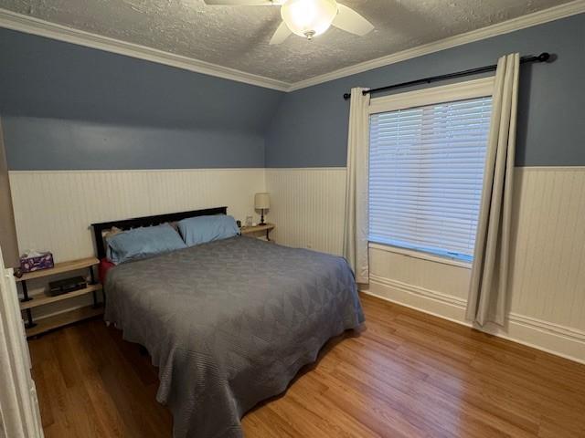 bedroom featuring a textured ceiling, ceiling fan, wood finished floors, and a wainscoted wall
