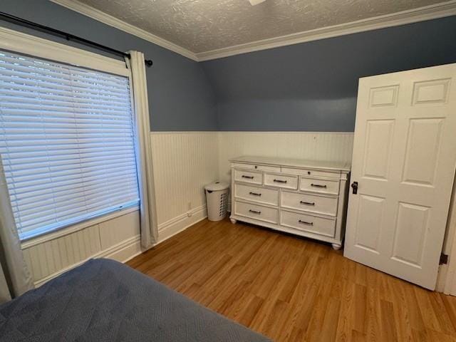 bedroom with crown molding, a textured ceiling, wood finished floors, and a wainscoted wall