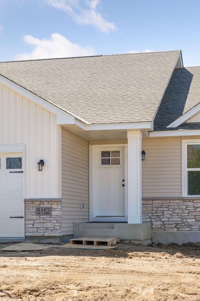 view of exterior entry featuring a shingled roof, board and batten siding, and stone siding