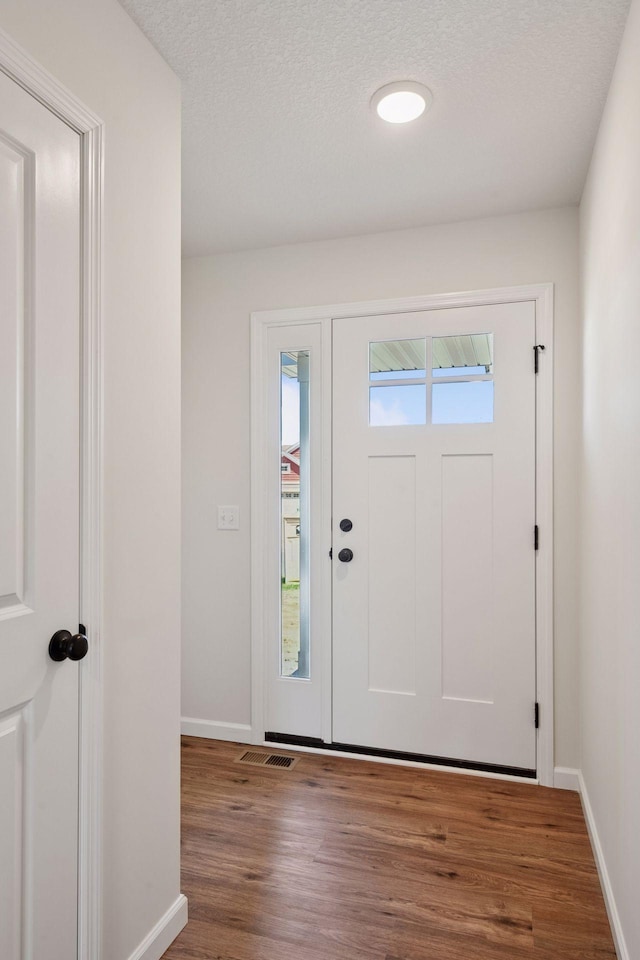 entrance foyer featuring baseboards, a textured ceiling, wood finished floors, and visible vents