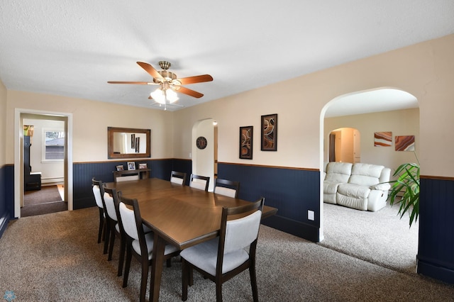 dining space with carpet flooring, arched walkways, and a wainscoted wall