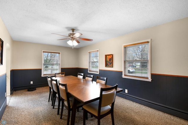 carpeted dining area with ceiling fan, wainscoting, wood walls, and a textured ceiling