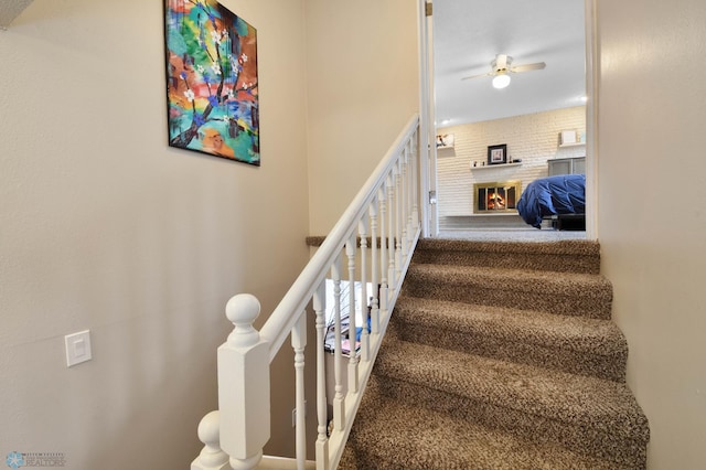 stairs with carpet floors, a ceiling fan, and a brick fireplace