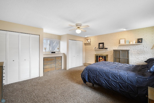 carpeted bedroom featuring two closets, a ceiling fan, a textured ceiling, and a fireplace