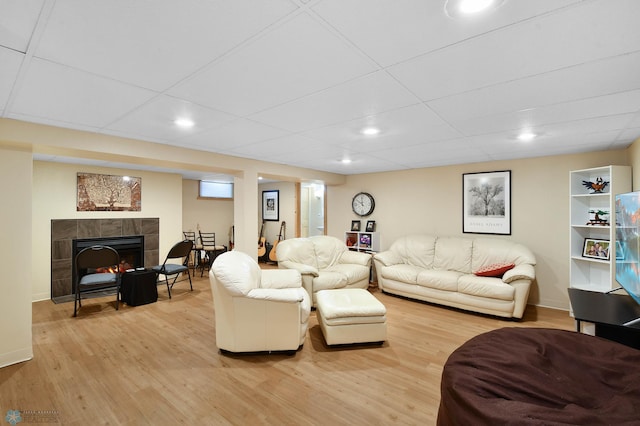 living area featuring baseboards, a tiled fireplace, and light wood finished floors