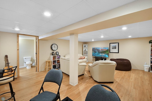 living area with baseboards, a drop ceiling, and light wood-style flooring