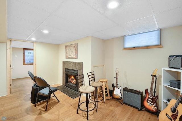 sitting room with wood finished floors, a tile fireplace, baseboards, a drop ceiling, and recessed lighting