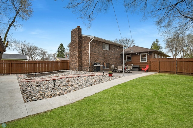 rear view of house featuring brick siding, a fenced backyard, a chimney, a patio area, and a lawn
