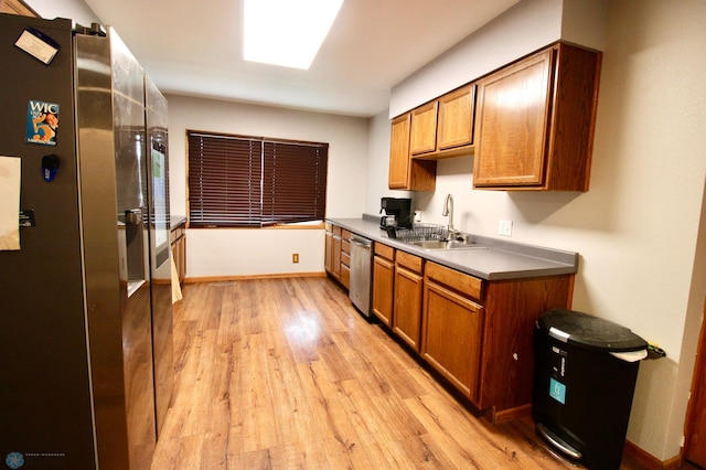 kitchen featuring brown cabinetry, baseboards, a sink, light wood-style flooring, and stainless steel appliances