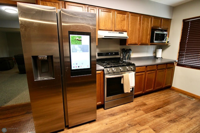 kitchen featuring brown cabinets, stainless steel appliances, light wood-type flooring, under cabinet range hood, and visible vents