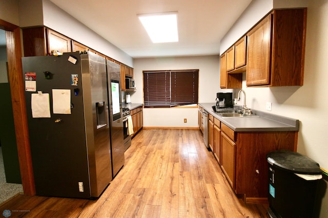 kitchen featuring appliances with stainless steel finishes, brown cabinetry, a sink, and light wood-style flooring