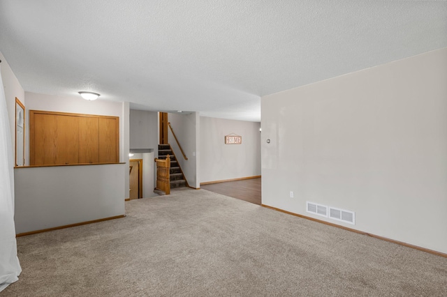 finished below grade area featuring stairway, carpet, a textured ceiling, and baseboards