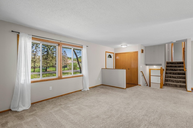 unfurnished room with a textured ceiling, carpet floors, and baseboards