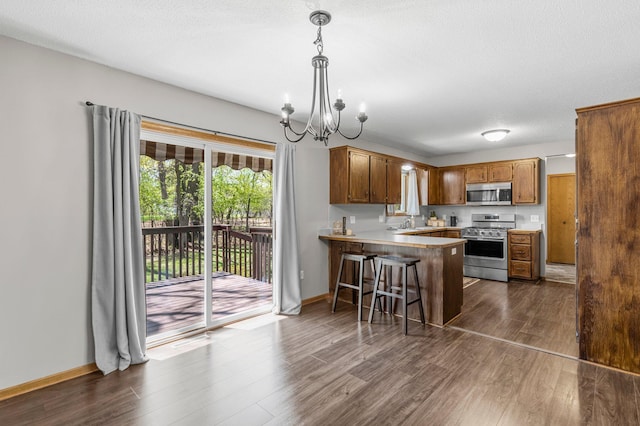 kitchen featuring appliances with stainless steel finishes, a peninsula, a chandelier, and dark wood-type flooring