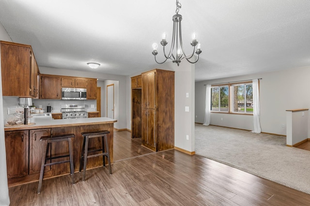 kitchen featuring appliances with stainless steel finishes, open floor plan, wood finished floors, a chandelier, and a peninsula