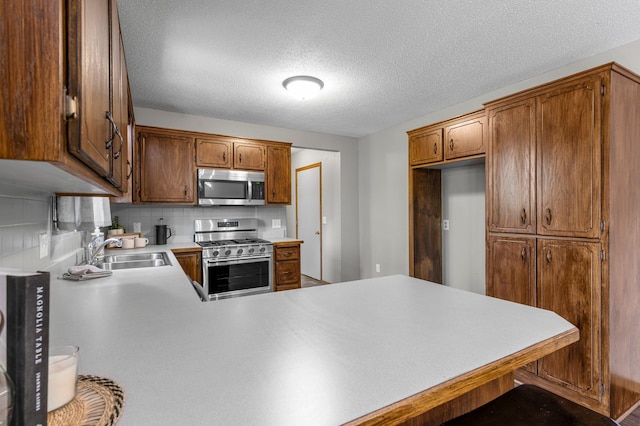 kitchen featuring appliances with stainless steel finishes, a sink, a peninsula, light countertops, and backsplash