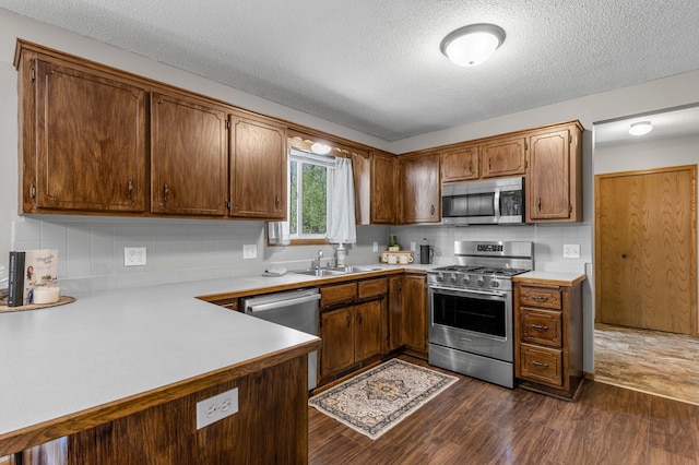 kitchen featuring stainless steel appliances, a sink, light countertops, dark wood finished floors, and a textured ceiling