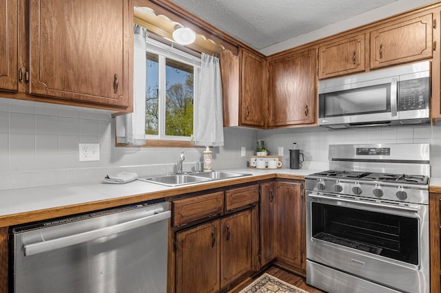 kitchen with appliances with stainless steel finishes, a sink, light countertops, decorative backsplash, and a textured ceiling
