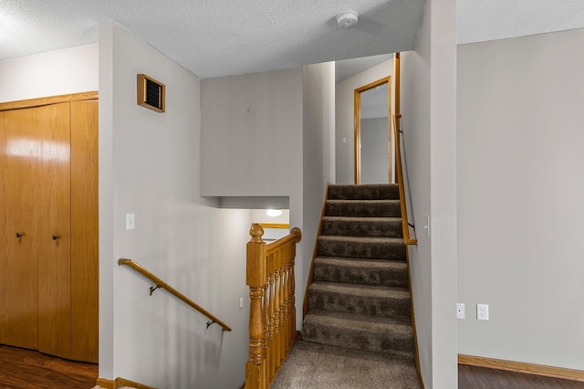 staircase with a textured ceiling, wood finished floors, and baseboards