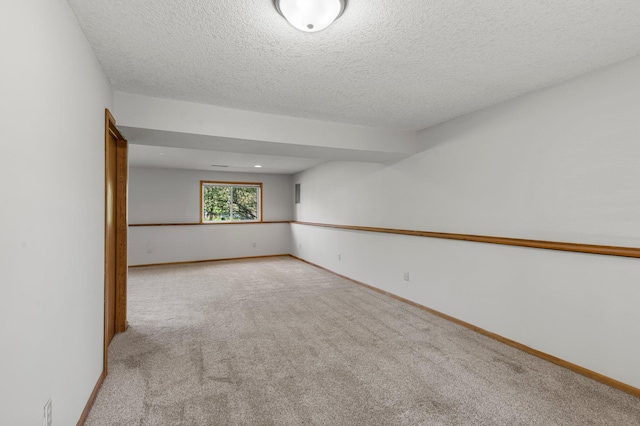 carpeted spare room featuring a textured ceiling and baseboards